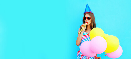 Portrait of cheerful young woman in a birthday cap with colorful balloons on a blue background
