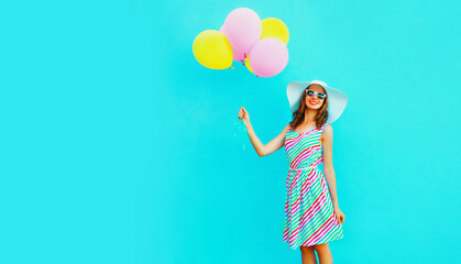 Portrait of beautiful happy smiling young woman with bunch of balloons wearing a colorful dress on blue background