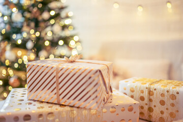 A lot of packing handmade gift boxes lying on the table near Christmas tree in the midst of golden lights, glowing garland, candle. Soft focus