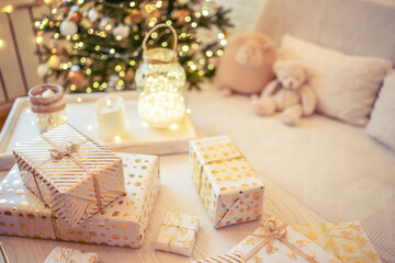 A lot of packing handmade gift boxes lying on the table near Christmas tree in the midst of golden lights, glowing garland, candle. Soft focus