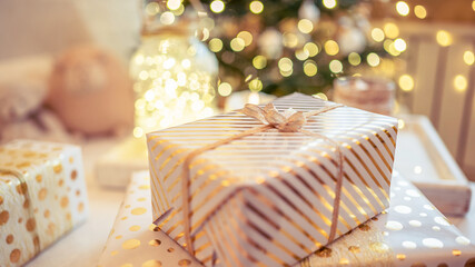 A lot of packing handmade gift boxes lying on the table near Christmas tree in the midst of golden lights, glowing garland, candle. Soft focus. 16:9