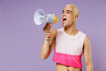 Young latin gay man with make up wearing bright pink top hold scream in megaphone announces discount sale Hurry up isolated on plain pastel purple background. People lifestyle fashion lgbtq concept.