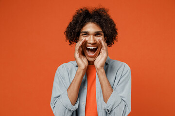 Young promoter black man 50s wearing blue shirt t-shirt scream hot news about sales discount with hands near mouth isolated on plain orange color background studio portrait. People lifestyle concept.