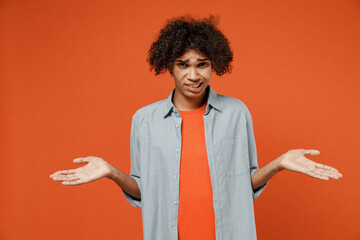 Young confused student black man 50s wearing blue shirt t-shirt shrugging shoulders looking puzzled, have no idea nothing to say spread hands isolated on plain orange color background studio portrait