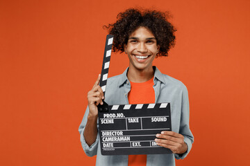 Young student black man 50s wearing blue shirt t-shirt look camera holding classic black film making clapperboard isolated on plain orange color background studio portrait. People lifestyle concept.