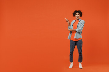 Full body smiling young student black man 50s wearing blue shirt t-shirt point index finger aside on copy space area isolated on plain orange color background studio portrait People lifestyle concept