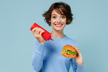 Young smiling caucasian fun cool woman 20s wearing casual sweater look camera biting eating burger...