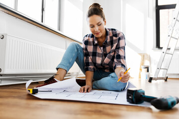 repair, people and real estate concept - woman with blueprint and pencil sitting on floor at home