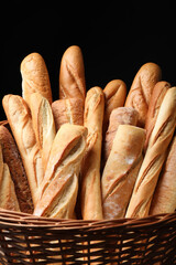Fresh tasty baguettes in basket against black background, closeup