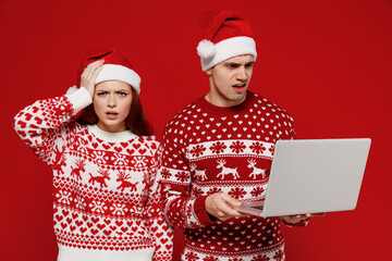 Young scared couple friends two man woman in sweater hat hold use work on laptop pc computer hold...