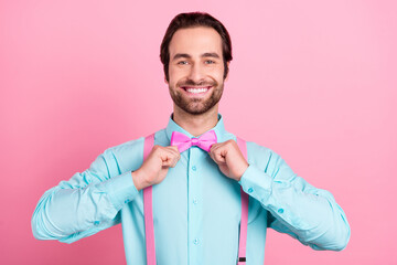 Photo of adorable charming young guy dressed teal clothes adjusting bowtie smiling isolated pink...