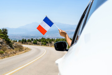 Woman holding France flag from the open car window driving along the serpentine road in the mountains. Concept