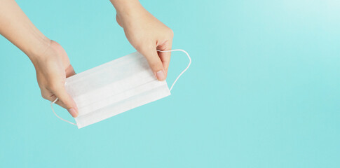 Hands holding white medical face mask on mint or Tiffany Blue background.