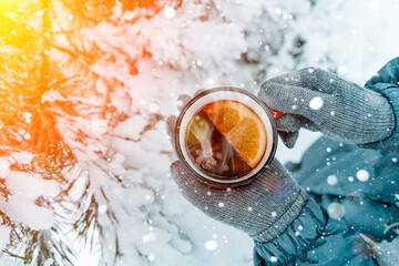 Mulled wine in the hands of a girl during a snowfall in the forest. Winter hot drinks with aromatic...