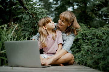 Young mother and child are playing on laptop in the garden