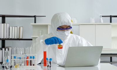 Epidemiological researchers in virus protective clothing mixing chemicals according to formulas obtained from computers. Working atmosphere in chemical laboratory.