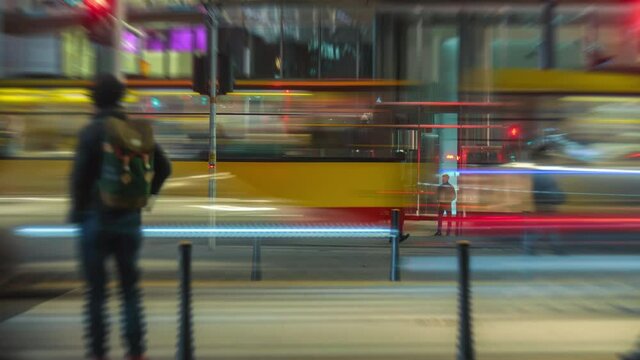Time-lapse busy crossroad car traffic jam unrecognizable people crossing street at night, trams moving fast in city in evening. Timelapse cars rush hour drive way, pedestrians crossing intersection