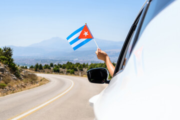 Woman holding Cuba flag from the open car window driving along the serpentine road in the mountains. Concept