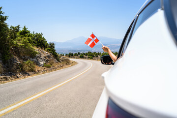 Woman holding Denmark flag from the open car window driving along the serpentine road in the mountains. Concept - obrazy, fototapety, plakaty