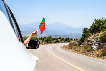 Woman holding Portugal flag from the open car window driving along the serpentine road in the...