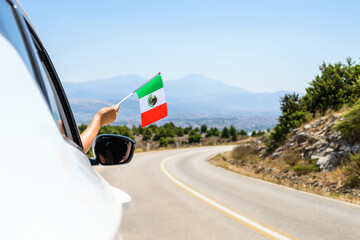 Woman holding Mexico flag from the open car window driving along the serpentine road in the...
