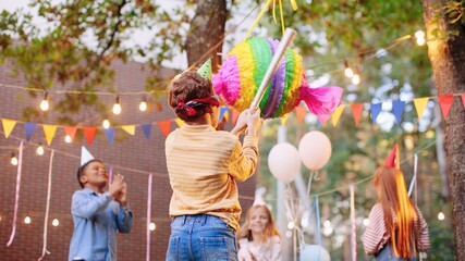 Children celebrating birthday in park. Group of children smash pinata with a bat at birthday party. Children having fun and playing
