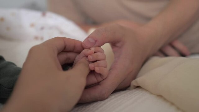 Concept of love and family. Father and mother holding newborn kid, hand in hand. Childcare, maternity, parenthood. Playing with baby. Slow Motion, selective focus 