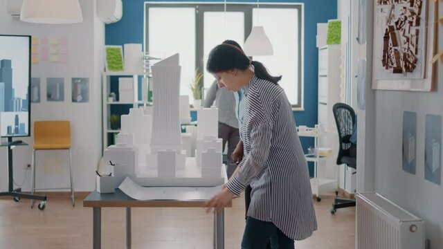 Team of diverse architects working together on building model design with blueprints. Women using sketch and maquette on table to plan construction layout and real estate structure.