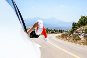 Woman driving a car holding santa claus hat from the open window. Trip on the serpentine road in...