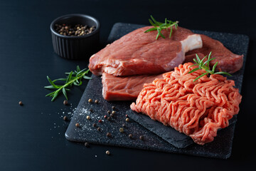 Fresh raw minced meat and cuts of beef, minced meat with herbs and spices on a black table