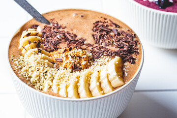 Chocolate smoothie bowl with banana, peanut butter and hemp seeds on white background. Raw vegan...