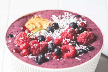 Berry smoothie bowl with raspberries, peanut butter and coconut on white tile background. Raw vegan food concept.