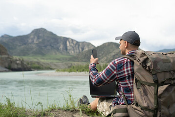 one hiker man using smart phone on the beach of mountain river