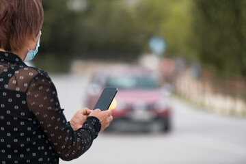 Woman holding smartphone in hands and messaging in online in street. Back view