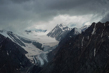 Dramatic landscape with glacier. Atmospheric minimalism with large snow mountain tops, dark glacier in dramatic sky.