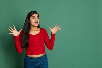 Exicted young adorable cute girl, student in casual style clothes posing isolated on dark green studio backgroud