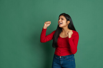 Exicted young adorable cute girl, student in casual style clothes posing isolated on dark green studio backgroud