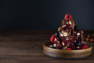Pieces of beet brownie with berries and chocolate on a dark background. Sugar, gluten and lactose free and vegan. Horizontal orientation, copy space.