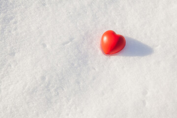 The red heart of the rubber antistress toy lies on the snow cover in sunny winter evening on sunset