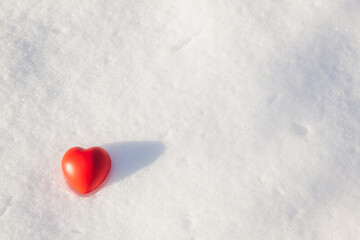 The red heart of the rubber antistress toy lies on the snow cover in sunny winter evening on sunset