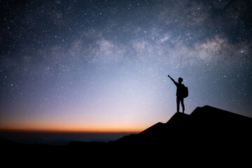 Silhouette of young traveler and backpacker raise your hand and point your finger at the stars and milky way in the sky. He enjoyed traveling and was successful when he reached the summit.