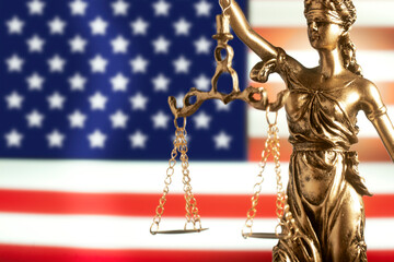 statue Themis representing justice and fairness with United States flag  unfocused in background