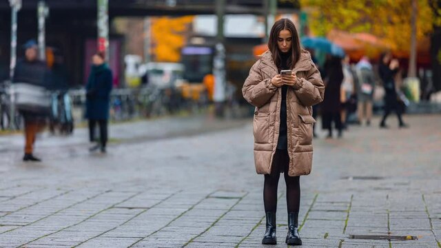 Time lapse of young woman using smart phone surfing social media, checking news, playing mobile games or texting messages staying on public street.