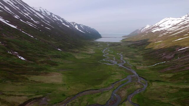 Dramatic Icelandic valley and mountain landscape, shot by drone. Snowy mountains and windy river below.