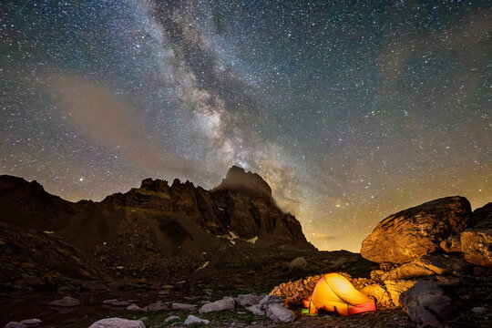 Milky Way galaxy stretching against night sky over lone illuminated tent in Maira Valley