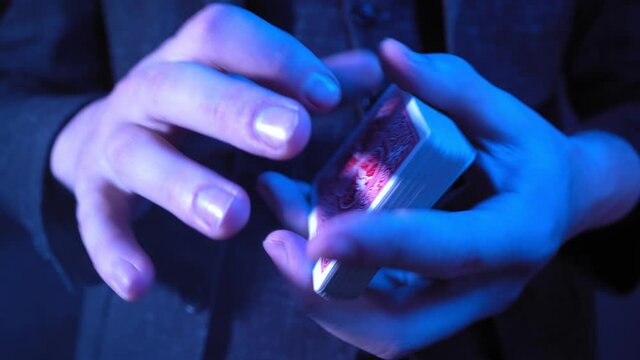 Close-up, Hands of a Magician Performing Tricks with a Deck of Cards. Blue Neon Lighting. Conjurer Shows Focus. Unrecognizable person. 