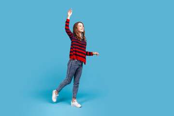 Full length portrait of happy smiling woman in sweater, stands with raised arm, looking into...