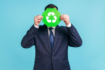 Unknown male person wearing official style suit hiding face behind green recycling sign, garbage...