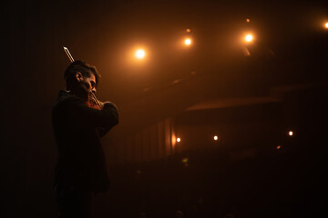 WIDE young aspiring musician playing violin on a stage of a large venue. Shot with 2x anamorphic...