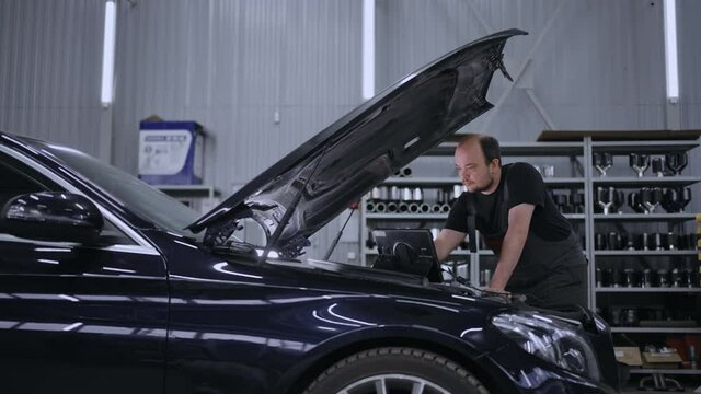 Car diagnostics and repair in the car service. The wizard stands at the hood with the computer to troubleshoot problems
